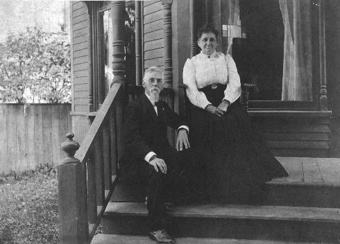 Emma smiles as she sits on a chair at the top of the broad porch steps, David casually on the first step below her, leaning against the rail.