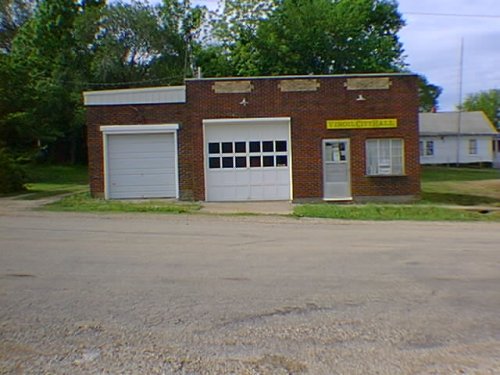 Small brick building with two bays; yellow sign says 'Virgil City Hall'