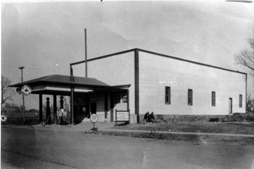 Long but narrow white building with dark trim at the edges, and an old-fashioned gas station portico attached to the front