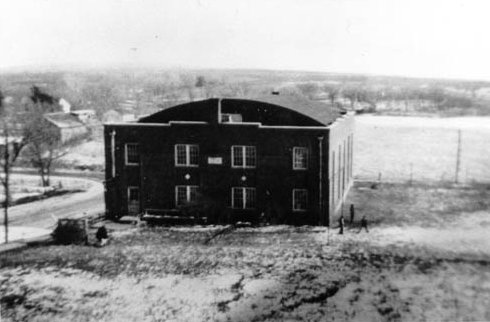 Large building with an aerodrome roof, surrounded on the front and right side by open ground