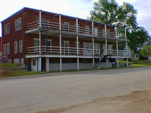 The hotel today, a  long red building with porches on the first and second floor (parking area below the first)