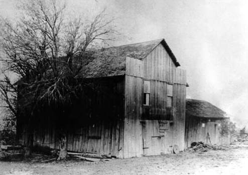 A small two-story building and attached one-story extension, with plain vertical wooden siding