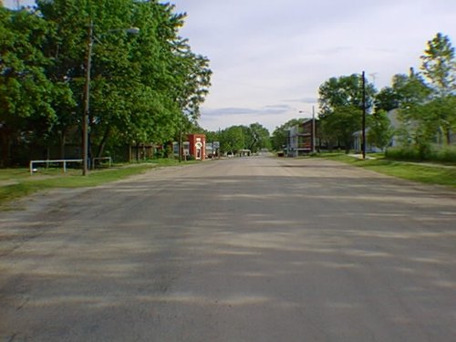 A simple asphalt road, no curbs, green trees, and the HalfStep in the distance on the right, shining in a patch of sun